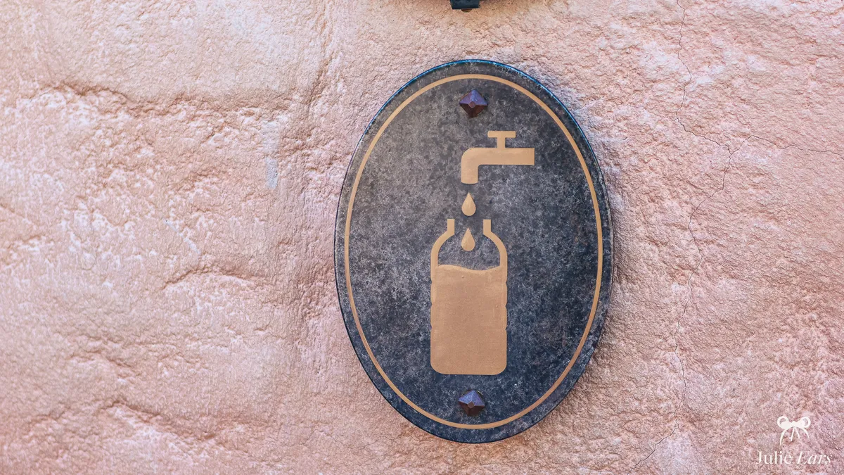 Oval plaque on a pink wall marking a water refill point at Disneyland Paris, with a gold tap and bottle pictogram