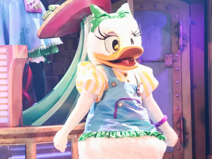 Daisy Duck en tenue jaune et bleue à nœud vert sur scène pendant le spectacle Minnie’s Dream Factory.