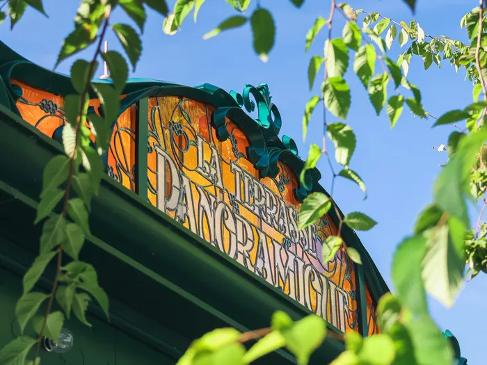 Decorated pediment of La Terrasse Panoramique seen from below, orange panel and green scrolls against a blue sky, Disneyland Paris