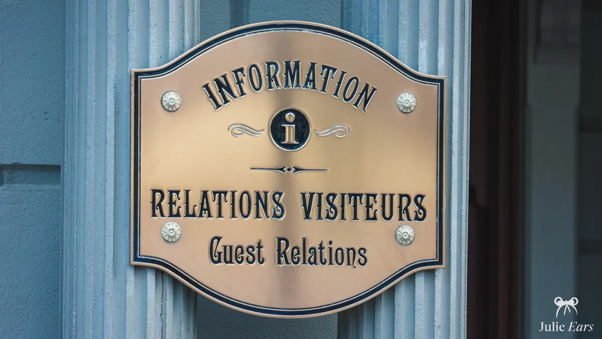 Brass plaque of the Disneyland Paris Guest Relations service (Relations Visiteurs), marked with the information symbol.
