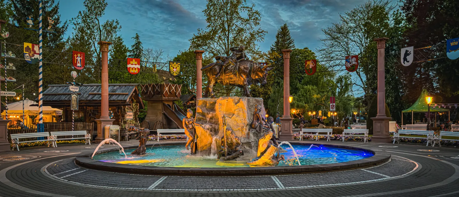 Fontaine illuminée aux sculptures dorées le soir, devant des maisons à colombages à Europa-Park