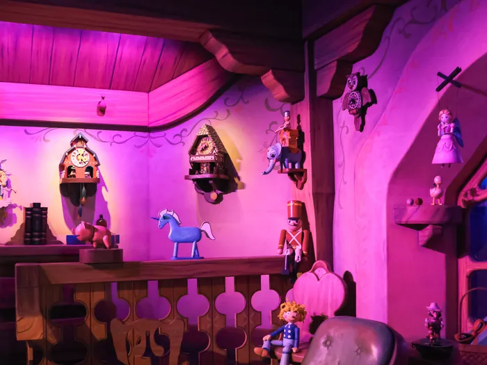 Décor de l’atelier de Geppetto avec coucous, jouets et pantins sur les étagères, éclairé en rose et violet