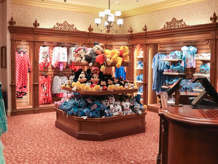Overview of the Disney Clothiers shop at Disneyland Paris: clothing rails and a central soft toy display.