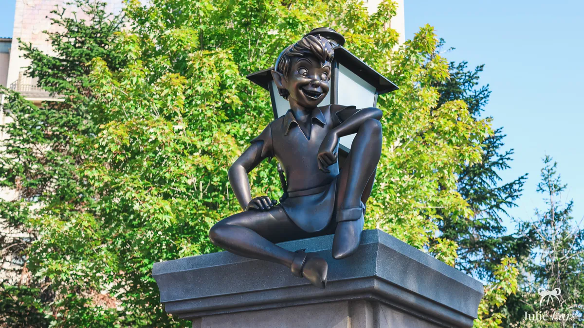Bronze statue of Peter Pan sitting on a pillar in front of a lantern, with a cheeky smile, in the Adventure Way garden at Disney Adventure World