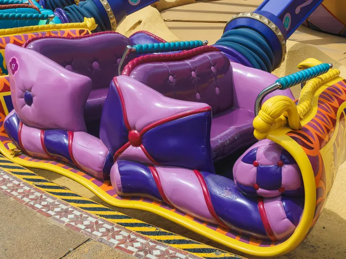 Nacelle vide en forme de tapis volant violet et jaune de l’attraction, aux banquettes matelassées