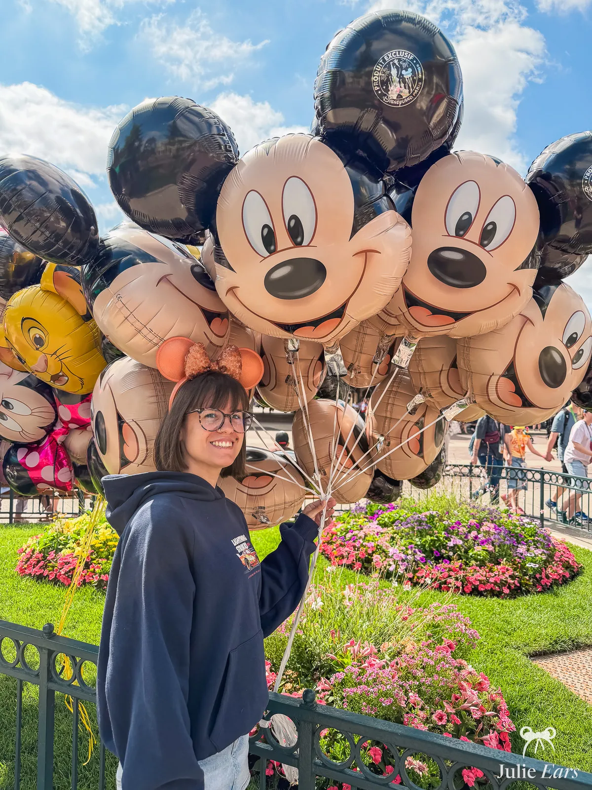 Bunch of Mickey head balloons held in a hand at Disneyland Paris, in front of the flower beds.
