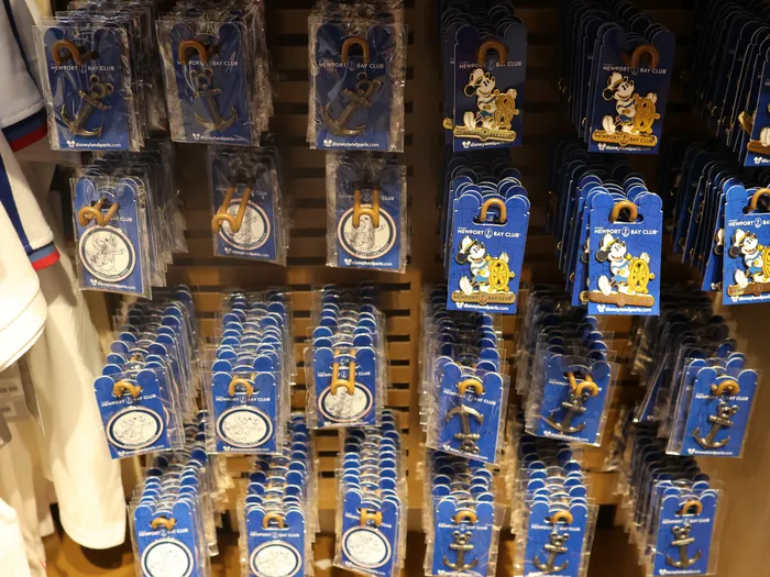 Display of pins on blue Newport Bay Club cards, with white bathrobes hanging on the left.