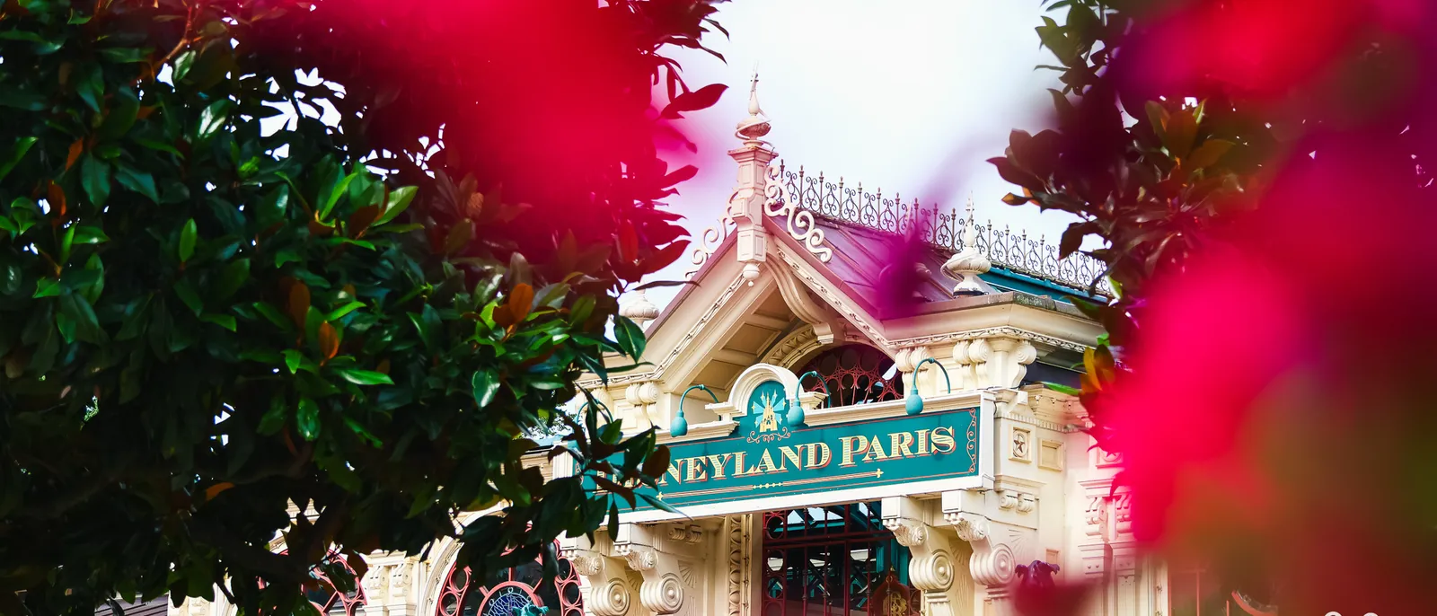 Façade de la gare Main Street U.S.A. avec l’enseigne Disneyland Paris, entrevue à travers un feuillage rose