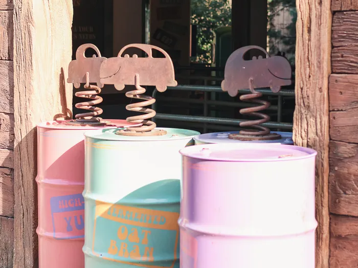 Three pastel cans topped with little metal cars on springs, in front of a wooden building at Cars Quatre Roues Rallye, Disneyland Paris