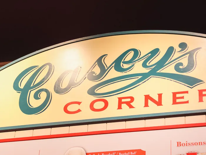 Enseigne jaune et verte Casey’s Corner illuminée le soir au-dessus du comptoir du restaurant.