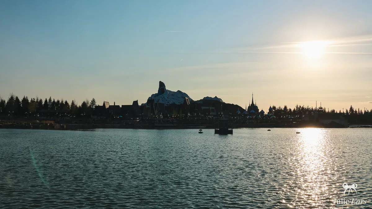 Vue du lac de Disney Adventure World au coucher du soleil, avec la silhouette de la montagne de World of Frozen à l’horizon à Disneyland Paris.