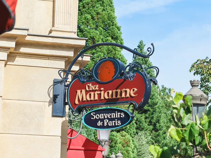 Red and gold hanging "Chez Marianne" sign, topped by a Marianne profile medallion, subtitled "Souvenirs de Paris", at Disneyland Paris