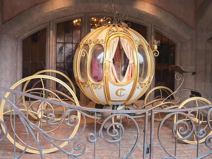 Carrosse doré en forme de citrouille frappé d’un « C » derrière une grille à l’entrée de l’Auberge de Cendrillon.