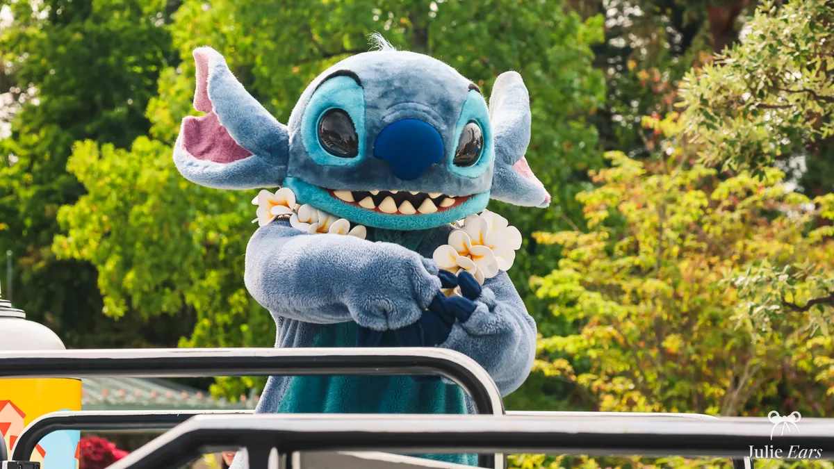 Stitch wearing a white flower garland smiles at visitors from his vehicle during a cavalcade at Disneyland Paris