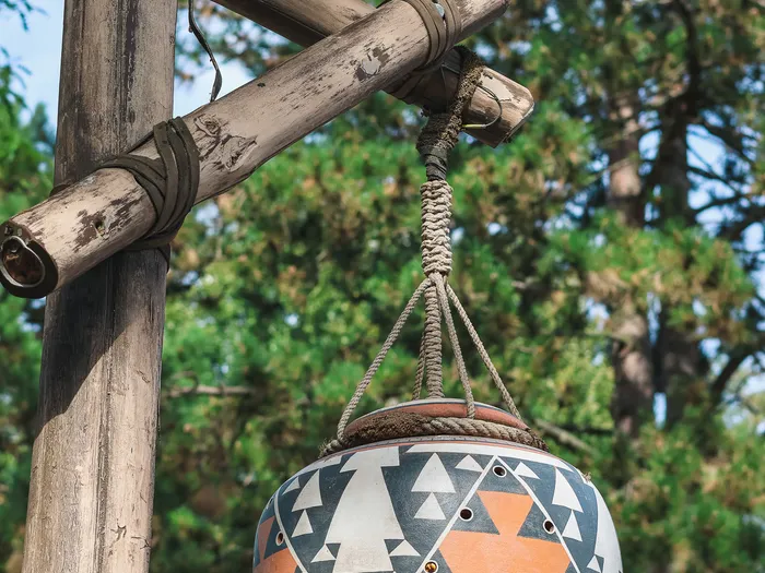 Orange pot with black and white geometric patterns and small holes, hanging from a log bracket near Pueblo Trading Post in Frontierland