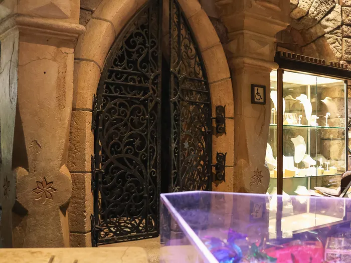 Inside the Merlin l’Enchanteur shop at Disneyland Paris: wrought-iron door under a Gothic stone arch, jewellery case and glassware counter.