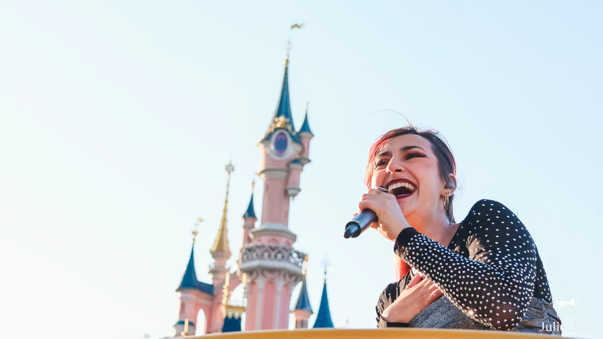 Singer in the middle of the Grand Orchestre finale, microphone in hand, in front of the castle at Disneyland Paris.
