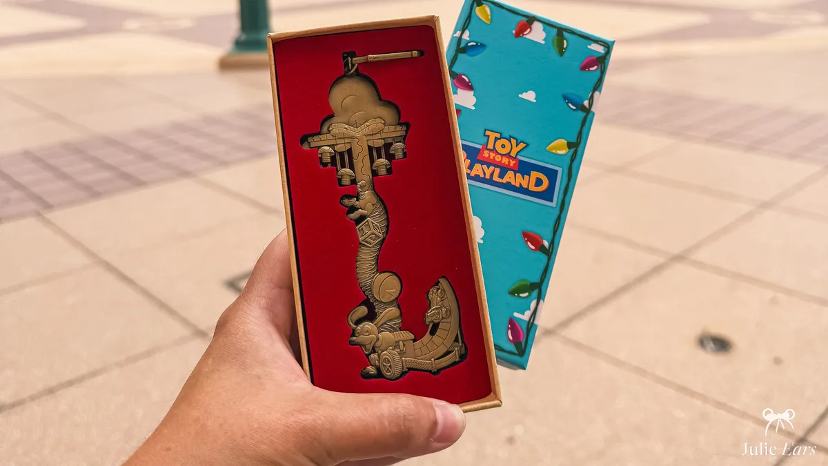 Toy Story Playland collector’s key with Slinky Dog in relief, in its red case held next to its blue box with fairy lights and clouds