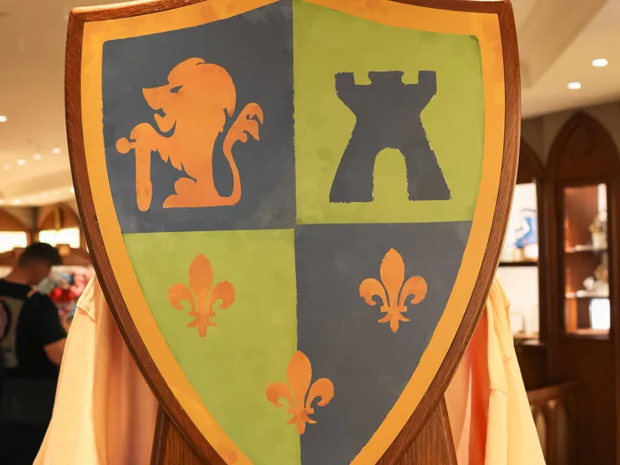 Blason décoratif bleu et vert orné d’un lion, d’une tour et de fleurs de lys.