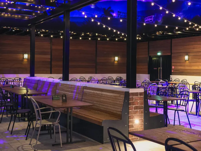 Salle du restaurant The Hollywood Gardens avec banquettes en bois, tables et guirlandes lumineuses sous plafond bleuté.