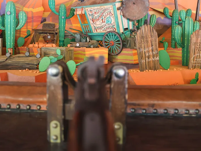 Canon de fusil pointé vers un décor de cactus et un chariot de tir au stand Rustler Roundup Shootin’ Gallery