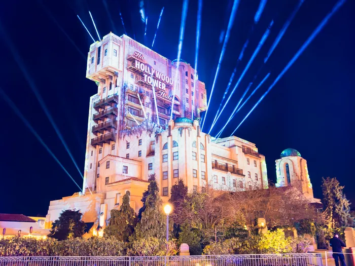 Façade de la Tower of Terror éclairée la nuit avec de longs faisceaux lumineux bleus dans le ciel