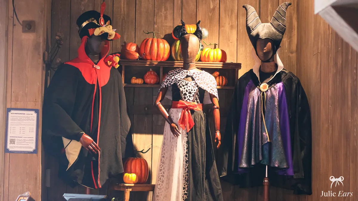 Three children’s Disney villain costumes in a Disneyland Paris shop at Halloween: Jafar, Cruella de Vil and Maleficent, with pumpkins behind