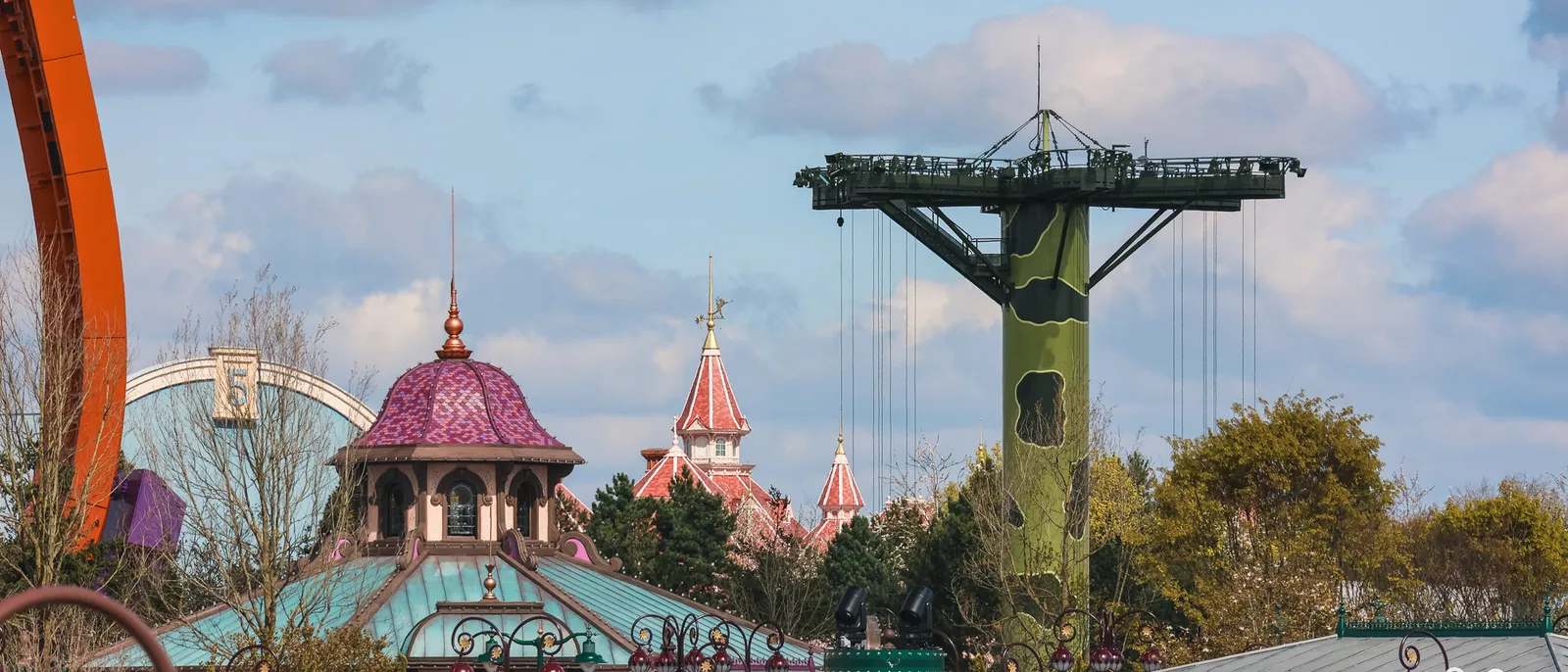 Grande grue de chantier verte dominant les toits du Parc Disney Adventure World, flèches du château au fond.