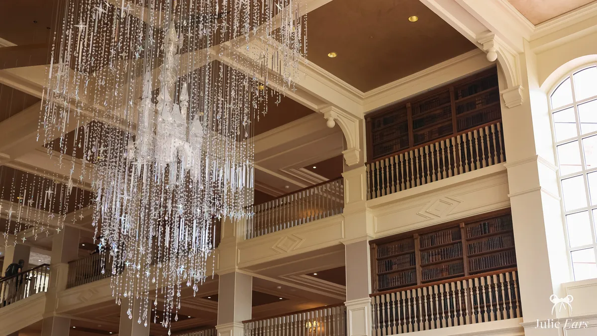 Crystal chandelier with a castle at its centre in the Disneyland Hotel lobby, surrounded by wooden balconies and book-lined shelves on several floors