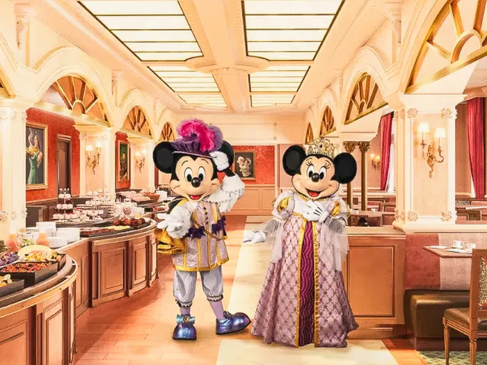 Mickey et Minnie en tenues royales dans la salle du restaurant Royal Banquet, buffet et décor doré à l’arrière-plan.