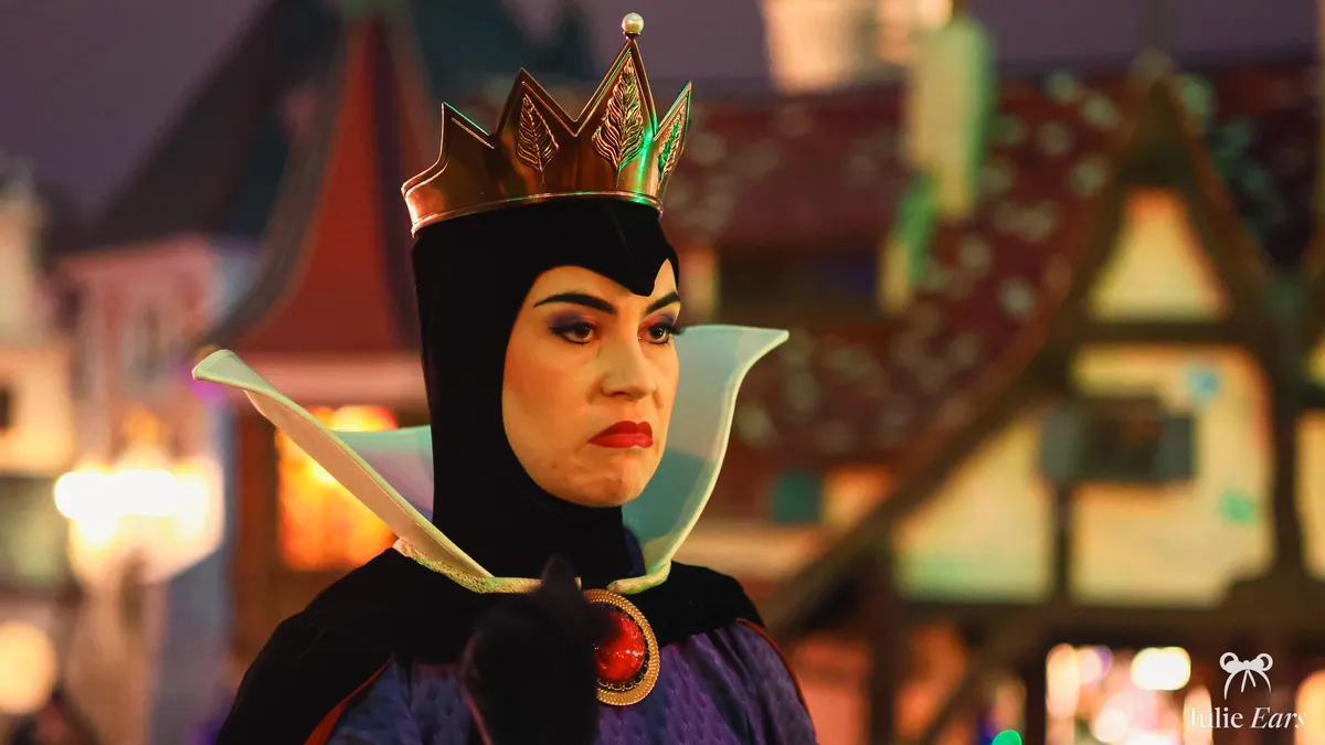 The Evil Queen from Snow White, with her golden crown and tall white collar, during an evening parade at Disneyland Paris.