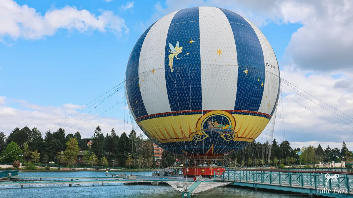 Blue and white PanoraMagique balloon with Tinker Bell, moored on Lake Disney at Disney Village, with pontoons and a footbridge