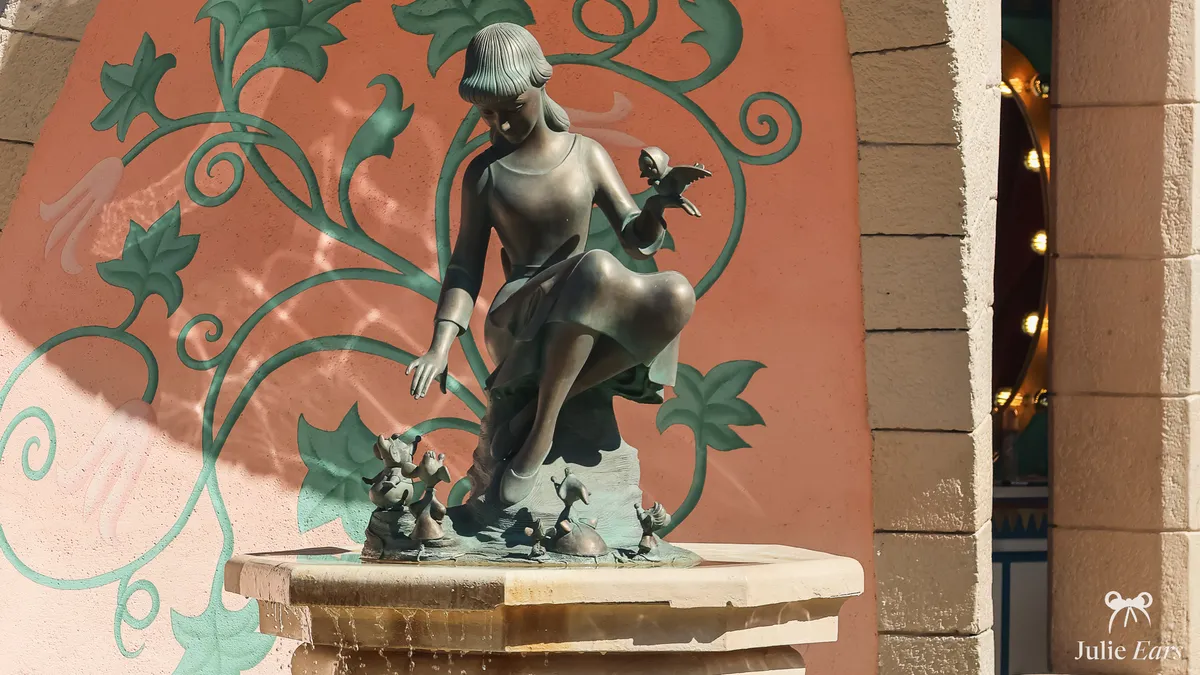 Bronze statue of Cinderella with a bird on her hand and mice at her feet, on the fountain of Auberge de Cendrillon at Disneyland Paris