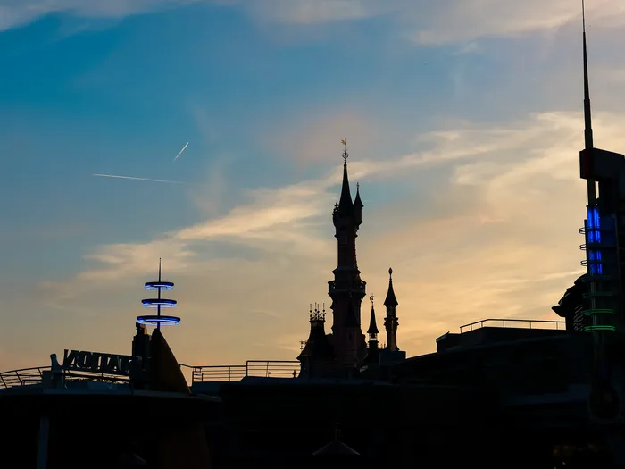 Silhouettes du château de la Belle au Bois Dormant et de Discoveryland sur un ciel de coucher de soleil orangé.