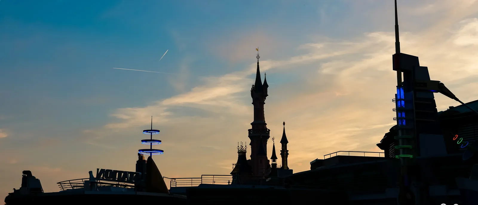 Silhouettes du château de la Belle au Bois Dormant et de Discoveryland sur un ciel de coucher de soleil orangé.