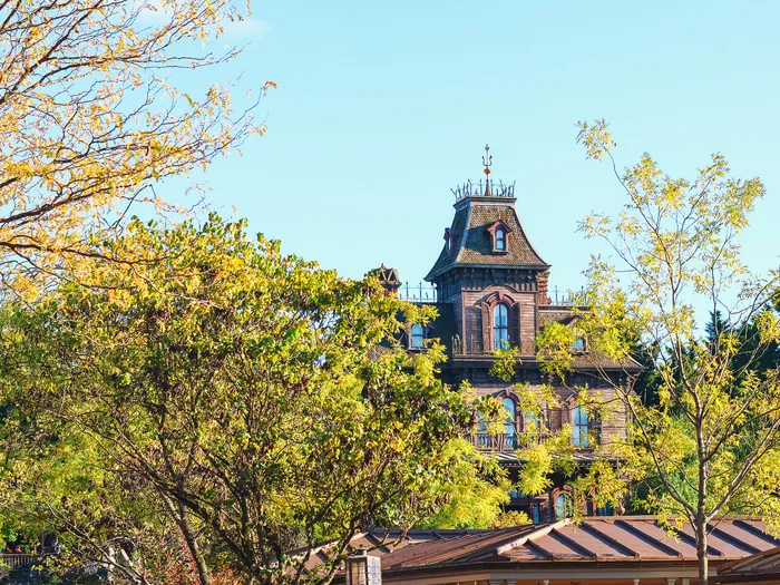 Le manoir de Phantom Manor émerge des feuillages jaunis de Frontierland sous un ciel bleu