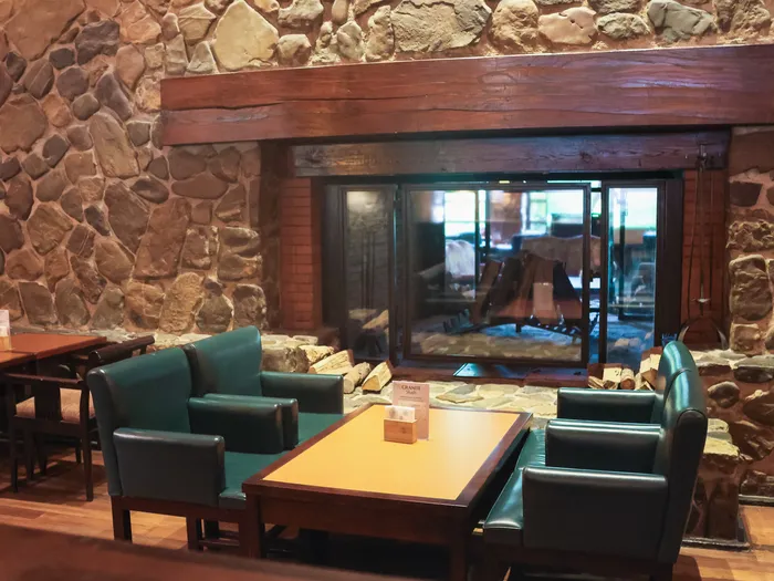 Grande cheminée en pierre et fauteuils en cuir vert du Redwood Bar, ambiance lodge du Disney Hotel Sequoia Lodge.