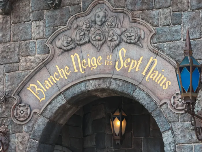 Enseigne dorée sculptée Blanche Neige et les Sept Nains encadrée de lanternes au-dessus du porche en pierre