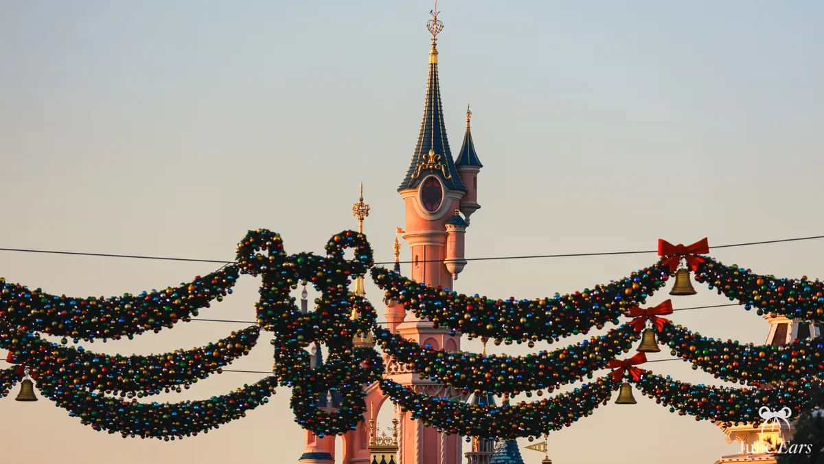 Guirlandes de Noël ornées de boules et de nœuds rouges devant une tourelle du château de la Belle au Bois Dormant à Disneyland Paris