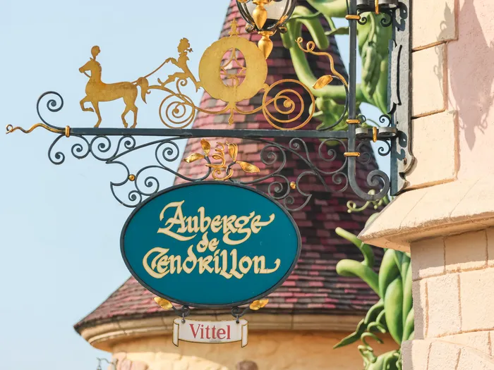 Enseigne en fer forgé de l’Auberge de Cendrillon, avec le carrosse doré, devant une tourelle du château à Fantasyland.