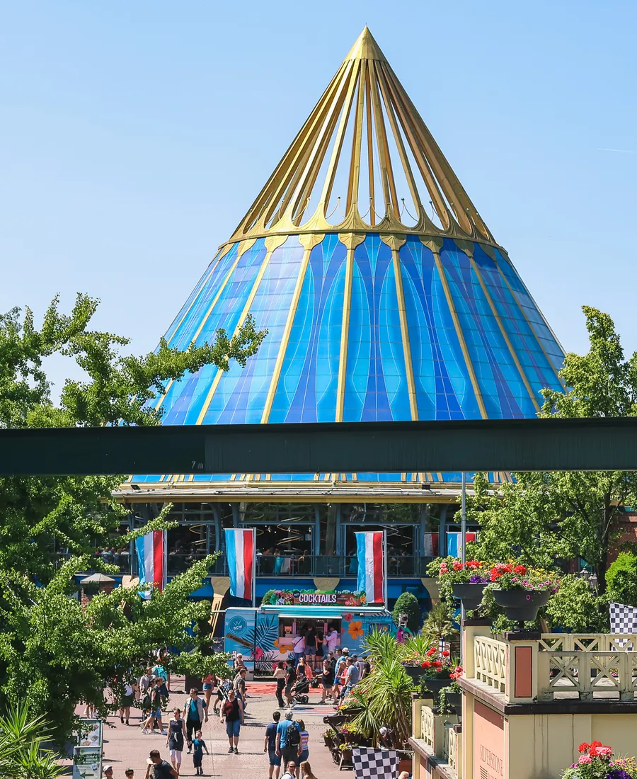 Grand dôme conique en verre bleu et or dominant une allée animée de visiteurs à Europa-Park
