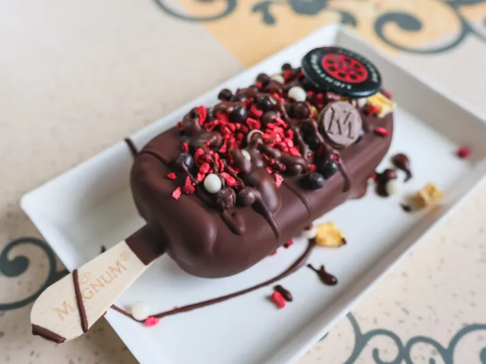 Bâtonnet glacé Magnum nappé de chocolat et parsemé d’éclats de framboise, sur une assiette blanche
