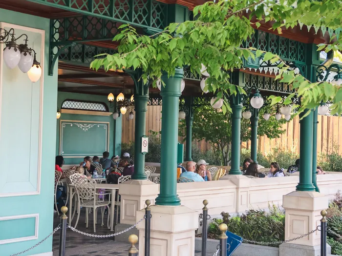 Covered terrace of La Terrasse Panoramique at Disneyland Paris, green columns and white tables where visitors are having lunch