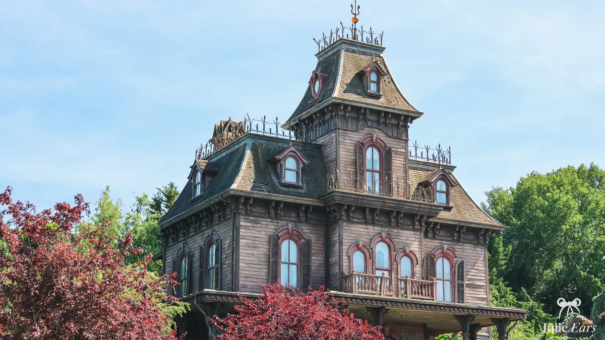 Phantom Manor in Frontierland at Disneyland Paris, with its tower, ornate windows and red-leaved trees in front, under a blue sky