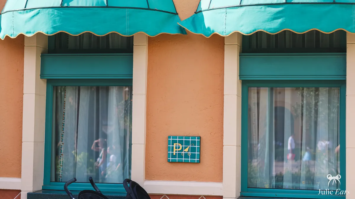 Orange Baby Care Centre facade at Disney Adventure World: scalloped aqua awnings, a "P" tile with a pushchair symbol and two parked pushchairs