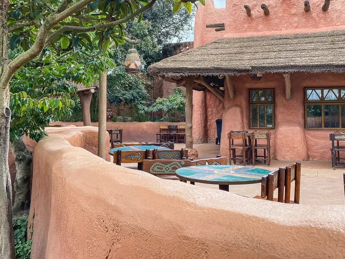 Terrasse du restaurant Hakuna Matata avec tables rondes peintes et tabourets devant une façade ocre à Adventureland