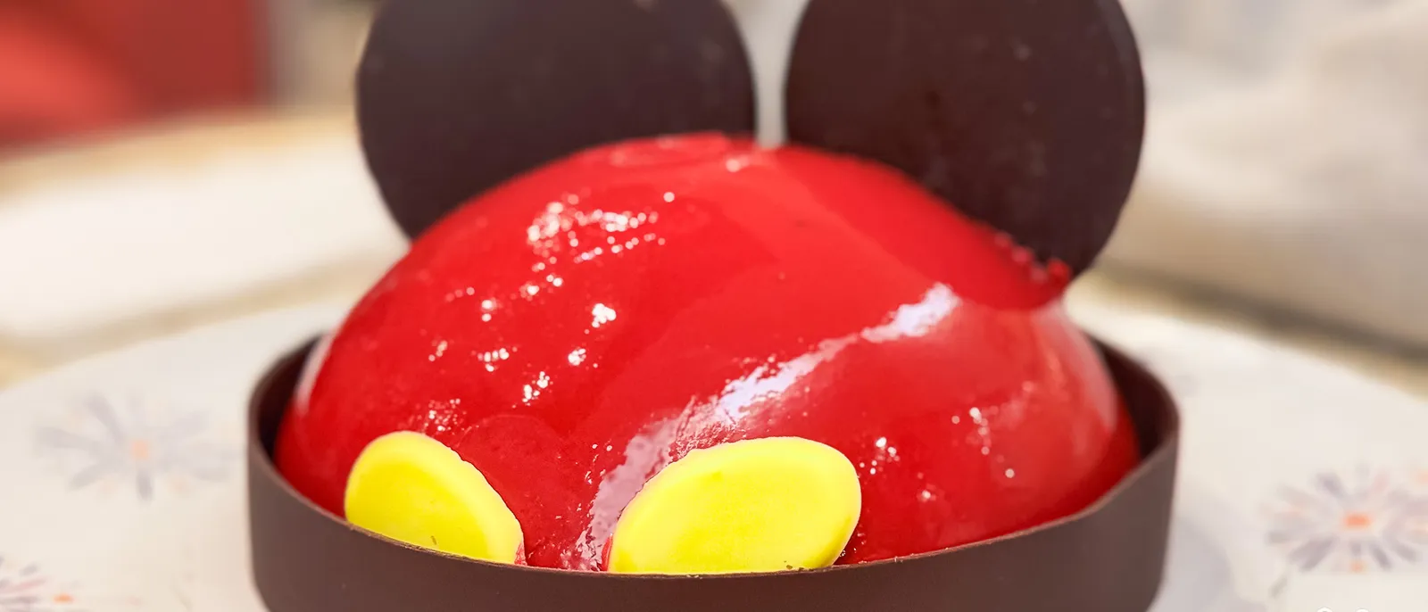 Gâteau en forme de tête de Mickey au glaçage rouge brillant, oreilles en chocolat et boutons jaunes.