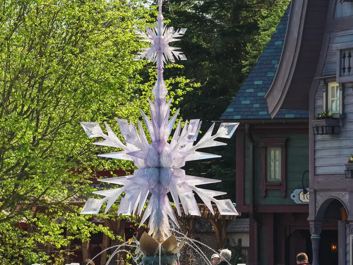 Grand flocon de glace translucide au sommet de la fontaine d’Arendelle, maisons de bois en fond à World of Frozen.