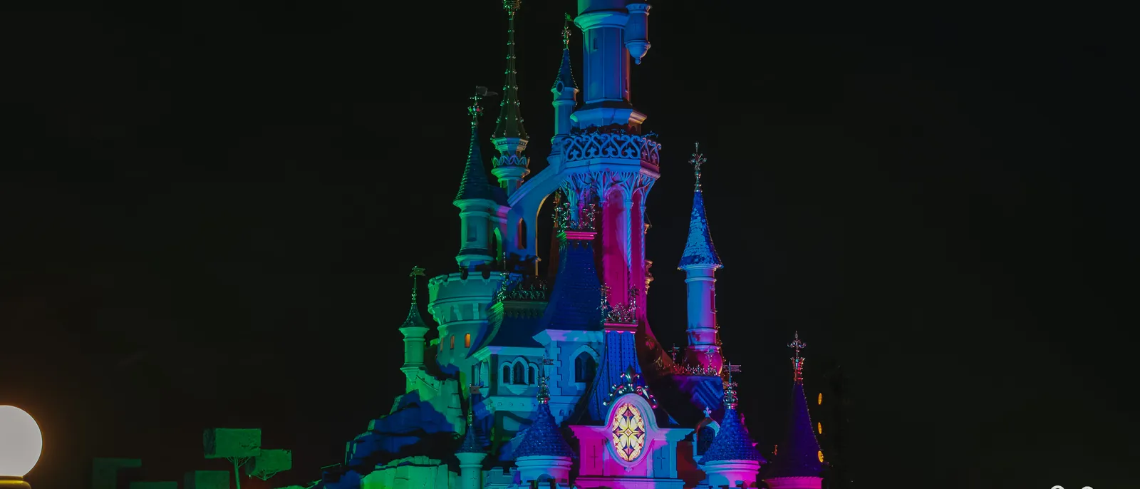 Le château de la Belle au Bois Dormant baigné de lumières roses, bleues et vertes dans la nuit à Disneyland Paris