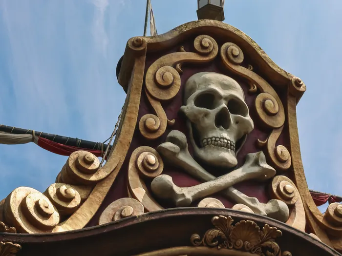 Crâne et os croisés sculptés entourés de volutes dorées au sommet du galion des pirates d’Adventureland.